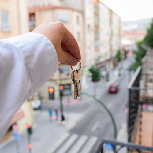 A man holds keys in a house with buildings in the background. Real state concept